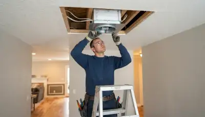Electrician installing a whole-house fan and insulated damper in a Denver, CO ceiling opening